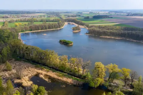 Malownicze jezioro z wyspami, otoczone lasami i polami. Idealne miejsce na romantyczne wypady w Polsce, gdzie można podziwiać przyrodę.