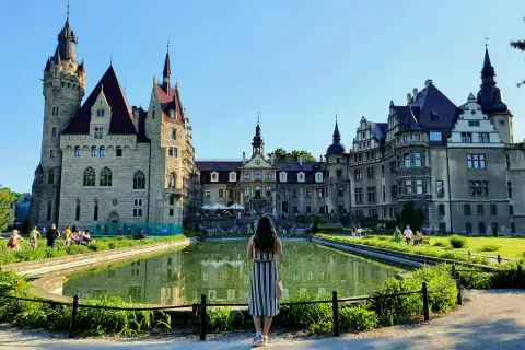 Kobieta podziwia zamek Moszna, jedną z największych atrakcji Opolszczyzny, z malowniczym stawem w tle.