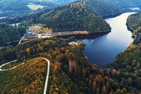 Malownicze jezioro Bystrzyckie otoczone lasami, z krętą drogą wijącą się po zboczu. W oddali widać zabudowania.