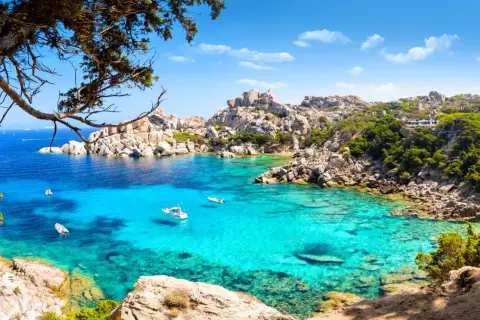 Turkusowa zatoka na Costa Smeralda, z łodziami i skalistymi brzegami porośniętymi zielenią.