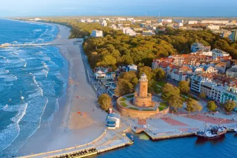 Widok na hotel i plażę nad morzem bałtyckim. Latarnia morska, molo i port z łodziami.