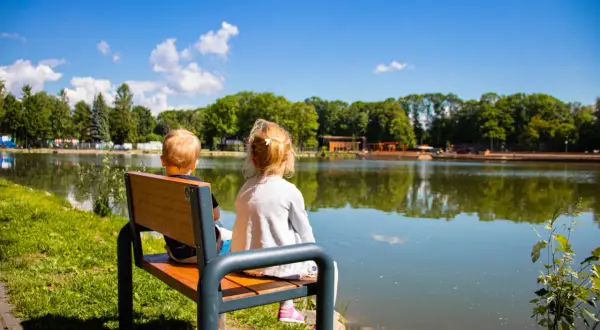 Dwoje dzieci siedzi na ławce, patrząc na spokojny zalew nowohucki.