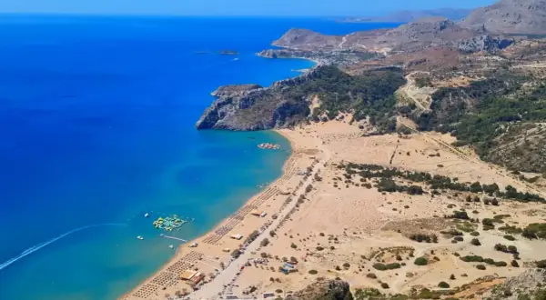Widok na zatokę z turkusową wodą, piaszczystą plażą pełną leżaków i parasoli, wodnym placem zabaw. Jedna z najlepszych plaż w Grecji.