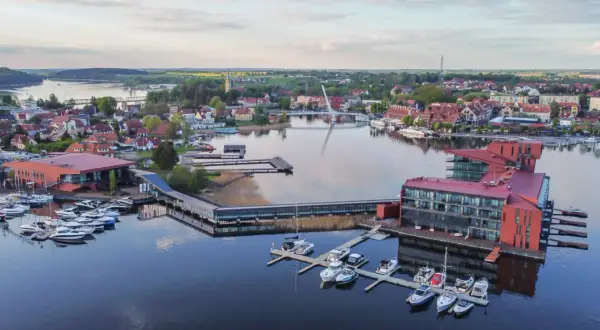Widok na nowoczesny hotel i przystań jachtową nad jeziorem. To jedno z najpiękniejszych miejsc na Mazurach, gdzie można podziwiać architekturę i wodę.