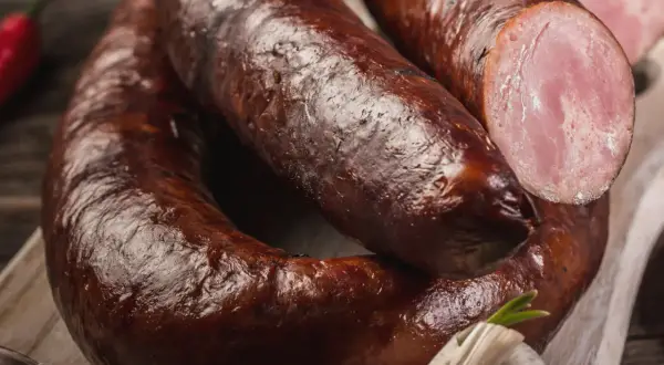 Kiełbasa lisiecka, wędzona, z widocznym przekrojem ukazującym różowe mięso. Obok czosnek i papryczka chili.