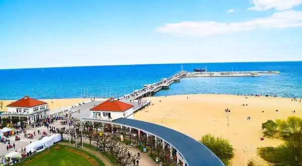 Słoneczna plaża w Sopocie z molo, budynkami i spacerującymi ludźmi.