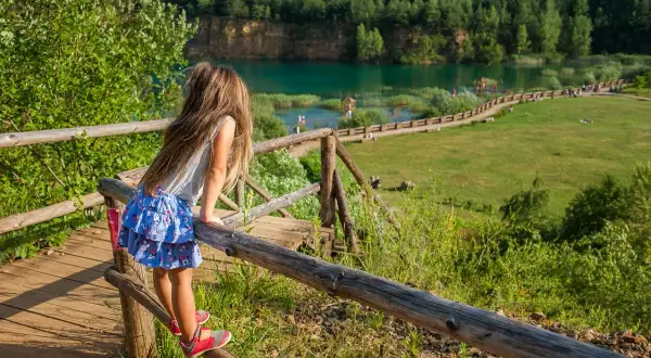 Dziewczynka na drewnianym pomoście podziwia turkusowe jezioro w Parku Gródek Jaworzno. Warto sprawdzić cenę wstępu, by cieszyć się tym widokiem.