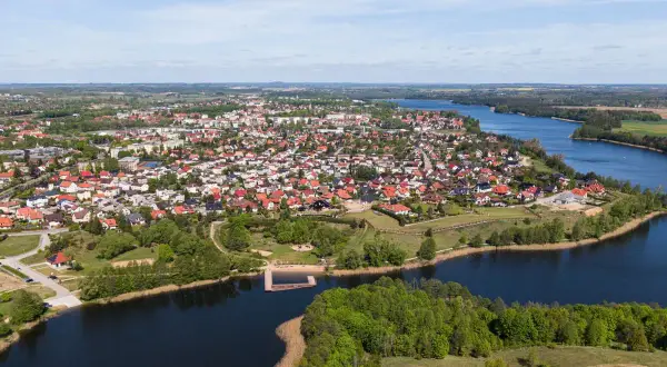 Widok z lotu ptaka na miasteczko nad jeziorem, z dachami domów i zielenią. To największy rynek w Polsce, tętniący życiem.