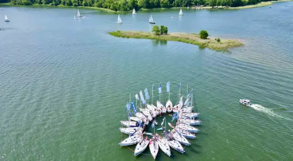 Piękne krajobrazy Polski: żaglówki tworzą okrąg na jeziorze, w tle las i mała wyspa.