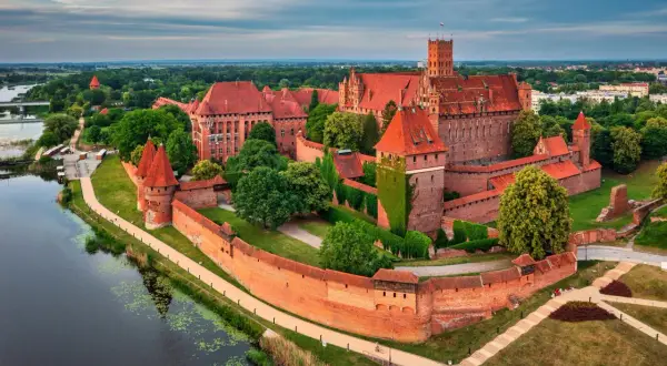 Malbork, największy zamek w Polsce, majestatycznie wznosi się nad rzeką Nogat. Czerwona cegła i strzeliste wieże tworzą imponujący widok.