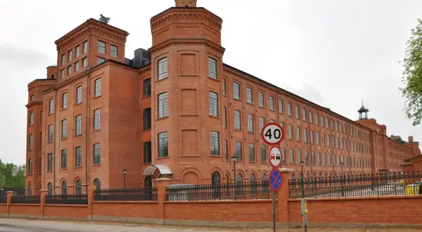 Imponujący, ceglany **księży młyn** w Łodzi, z charakterystycznymi wieżyczkami i długim rzędem okien. Obok znaki drogowe.