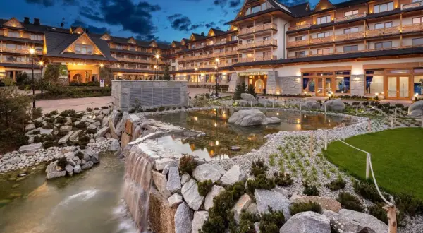 Elegancki hotel spa w górach z kaskadą wodną i stawem.