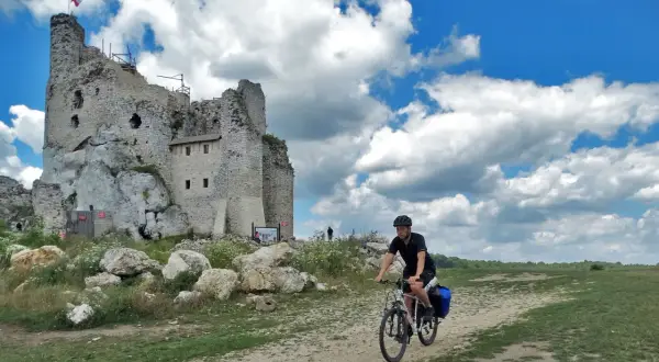 Rowerzysta przemierza malownicze **Jura Krakowsko-Częstochowska szlaki**, mijając ruiny zamku na skale.