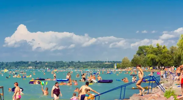 Tłum ludzi cieszy się latem na **jeziorze Balaton**. Kąpiel, pływanie na materacach i relaks na plaży.