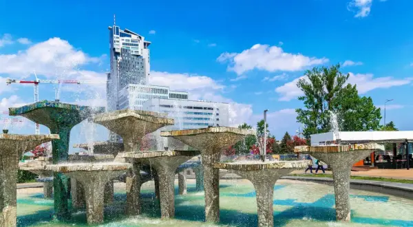 Fontanna z modernistycznymi budynkami w tle i błękitnym niebem.