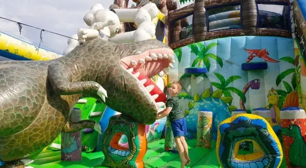 Chłopiec skacze na dmuchanym dinozaurze. Wspaniałe, ciekawe miejsca do 100 km od Katowic dla dzieci.