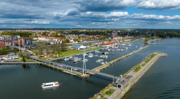Widok na jezioro, nad którym leży Giżycko, z mariną pełną łodzi, nowoczesnym mostem i spacerowiczami.