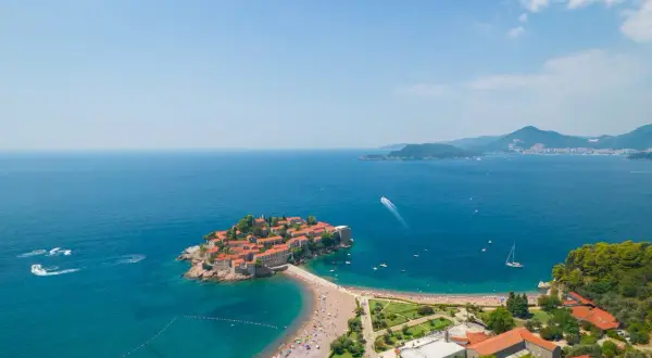 Sveti Stefan, Czarnogóra, z widokiem na turkusowe morze i zatłoczoną plażę.