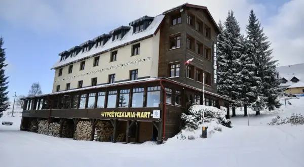 Zimowy hotel z drewnianymi elementami, idealny na zieleniec noclegi blisko stoku. Wokół śnieg i wysokie choinki.