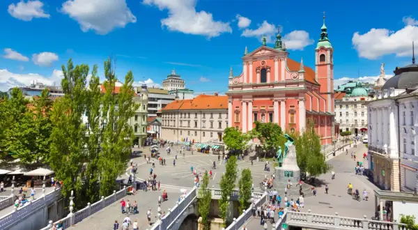 Tętniący życiem plac w Lublanie, stolicy Słowenii, z różową katedrą i mostami pełnymi ludzi.