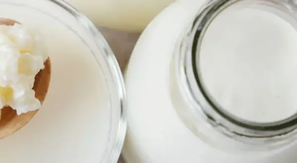 Ziarna żętycy na łyżce obok szklanki i butelki z mlekiem. To naturalny probiotyk.