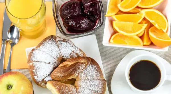 Idealne śniadanie kontynentalne: świeże croissanty, sok pomarańczowy, kawa, owoce i dżem.