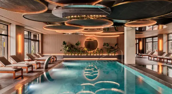 Luksusowy basen w karpacz hotel spa. Woda lśni, otoczona leżakami i zielenią. Nowoczesny design sufitu z podświetleniem.