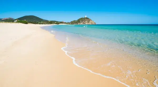 Piękne plaże Cagliari, z turkusową wodą i złotym piaskiem, zapraszają do relaksu. W oddali widać wieżę na wzgórzu.