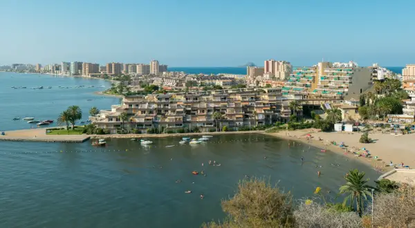 Widok na La Mangę z plażą, budynkami mieszkalnymi i łodziami na wodzie.