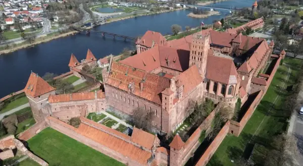 Potężny zamek w Malborku, największy zamek w Europie, rozciąga się wzdłuż rzeki. Jego ceglane mury i wieże świadczą o bogatej historii.