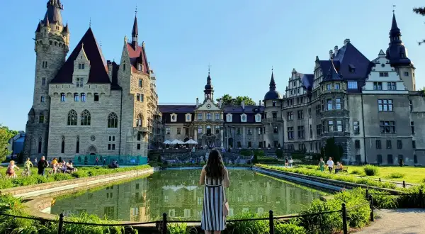 Kobieta podziwia zamek Moszna, jedną z największych atrakcji Opolszczyzny, z malowniczym stawem w tle.