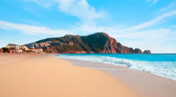 Piękna plaża Kleopatry z turkusową wodą i skalistym cyplem, na którym widać ruiny zamku.