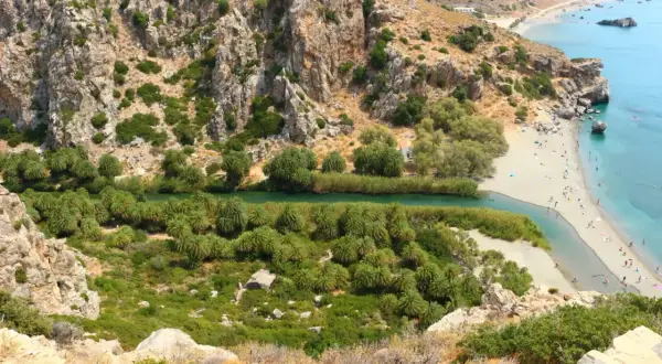 Malowniczy widok na plażę Preveli z rzeką, palmami i turkusowym morzem.