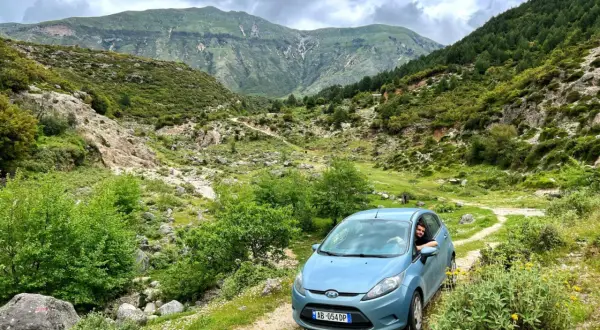 Podróż przez górzyste tereny Albanii samochodem. Błękitny Ford Fiesta na piaszczystej drodze wśród zieleni i skał.