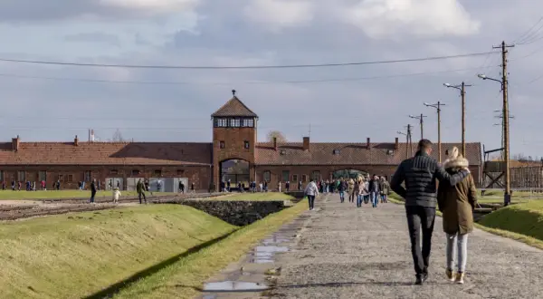 Spacer po terenie Państwowego Muzeum Auschwitz-Birkenau w Oświęcimiu. Ludzie zwiedzają teren dawnego obozu.