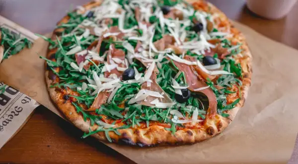 Pyszna pizza parma z rukolą, oliwkami i parmezanem, podana na papierze.