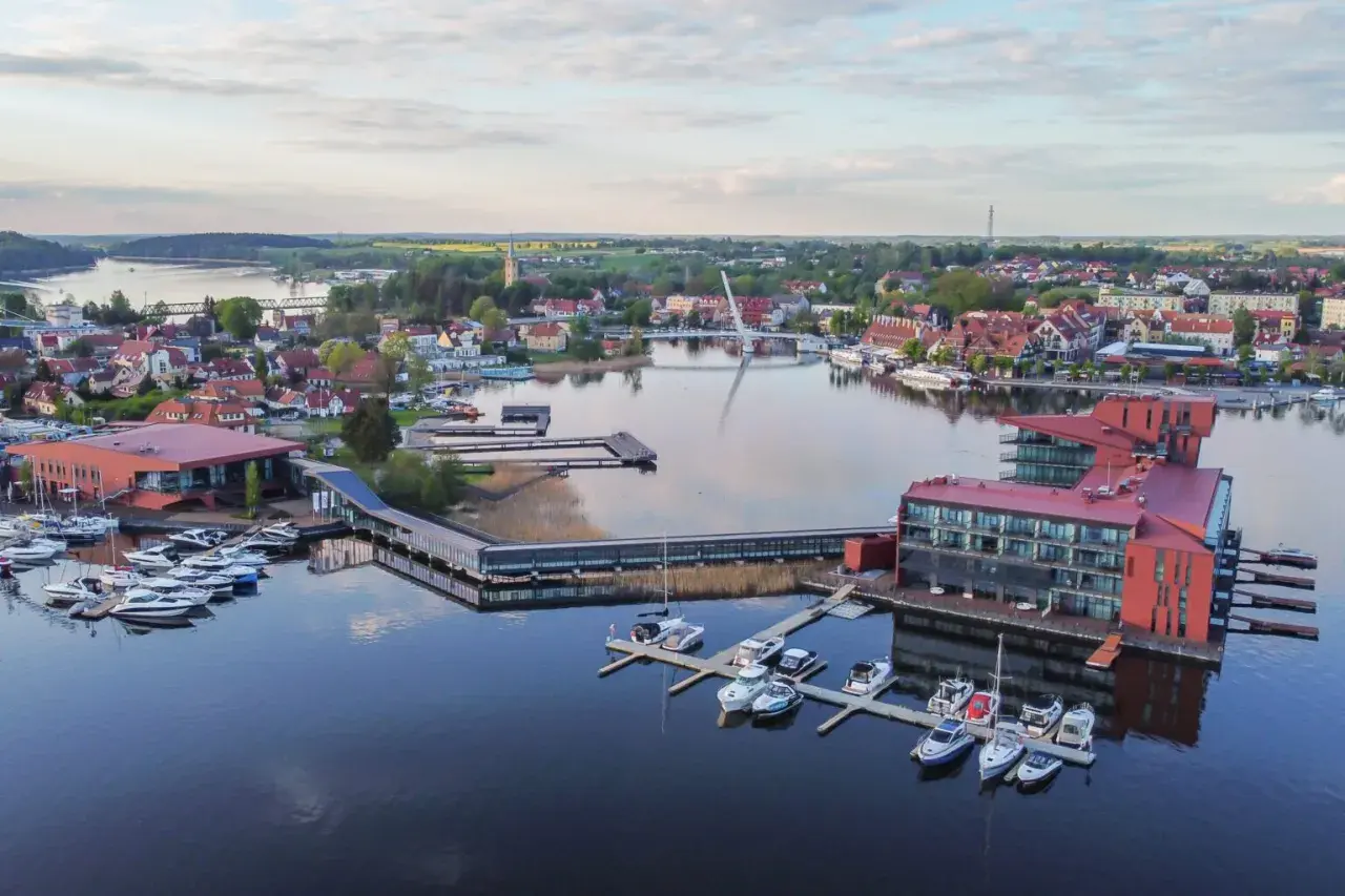 Widok na nowoczesny hotel i przystań jachtową nad jeziorem. To jedno z najpiękniejszych miejsc na Mazurach, gdzie można podziwiać architekturę i wodę.