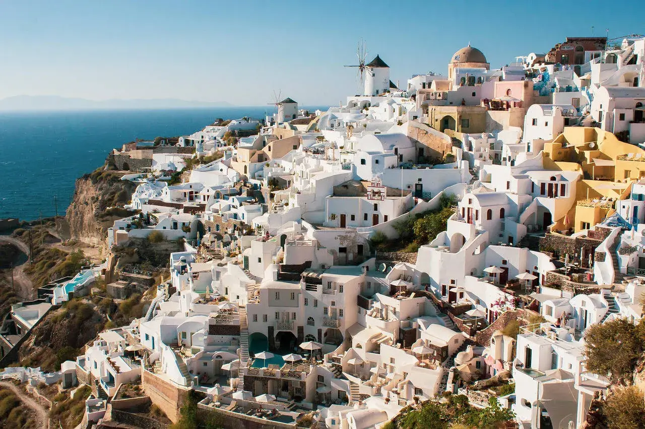 Malownicze białe domy Santorini, w tym wiatraki, wznoszą się na klifie nad morzem. Widok przypomina starożytne Akrotiri.