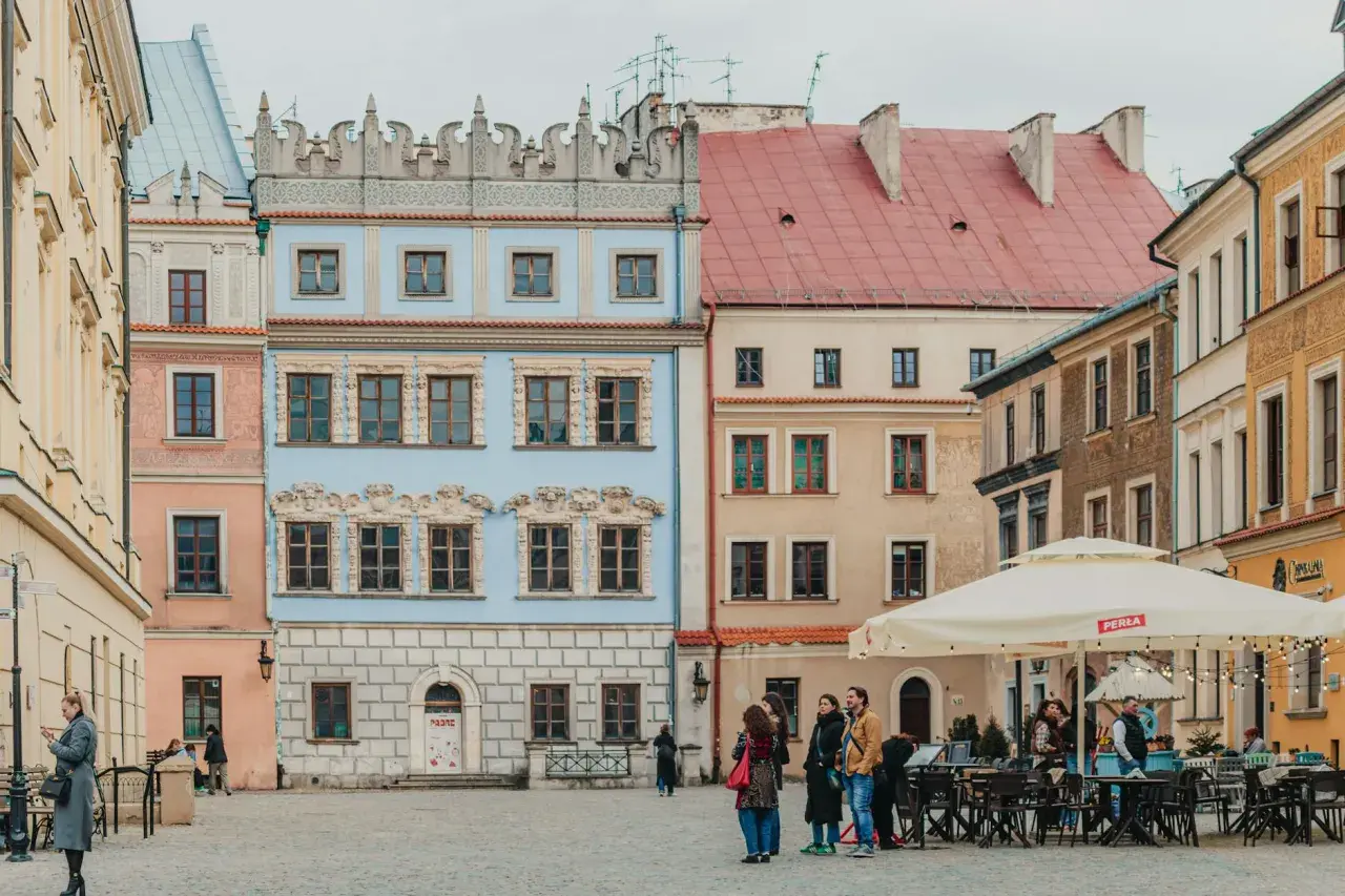 Kolorowe kamienice na Rynku Starego Miasta w Lublinie, z ludźmi spacerującymi i siedzącymi w ogródku kawiarnianym.
