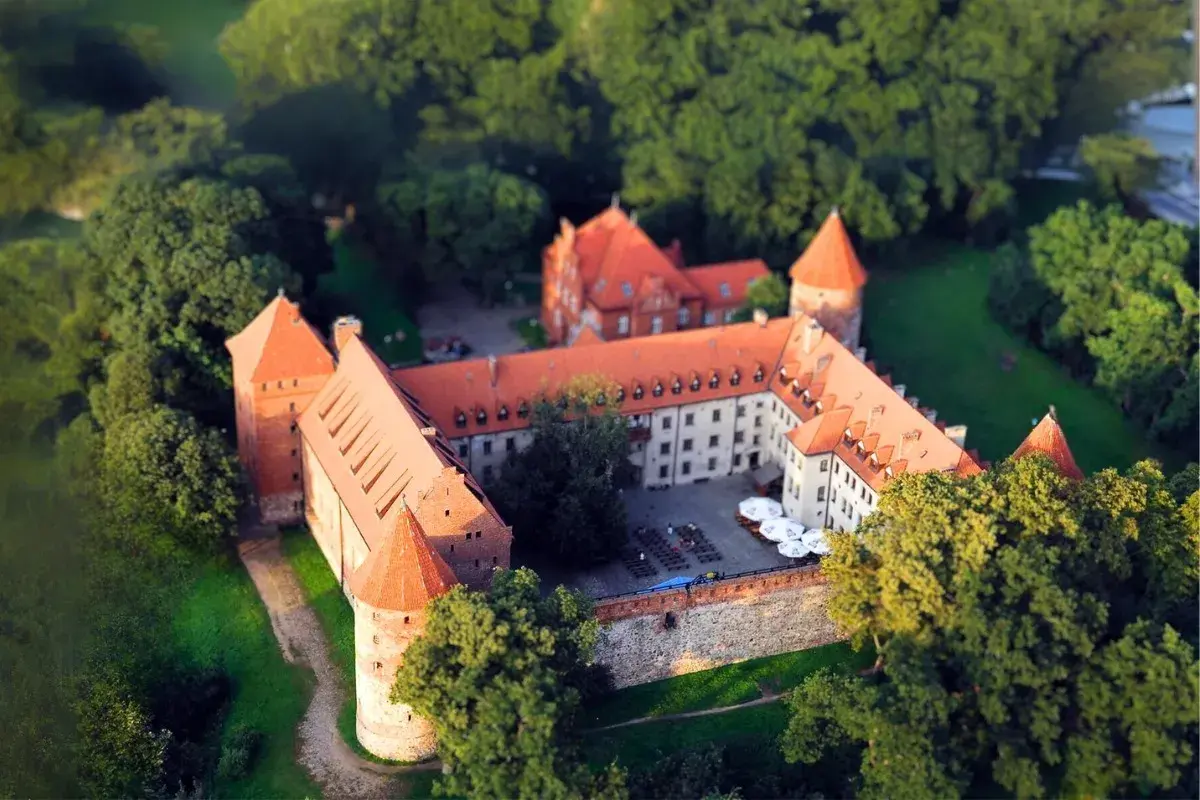 Zamek w Bytowie otoczony zielenią, z czerwonymi dachami i wieżami, wygląda jak z bajki.