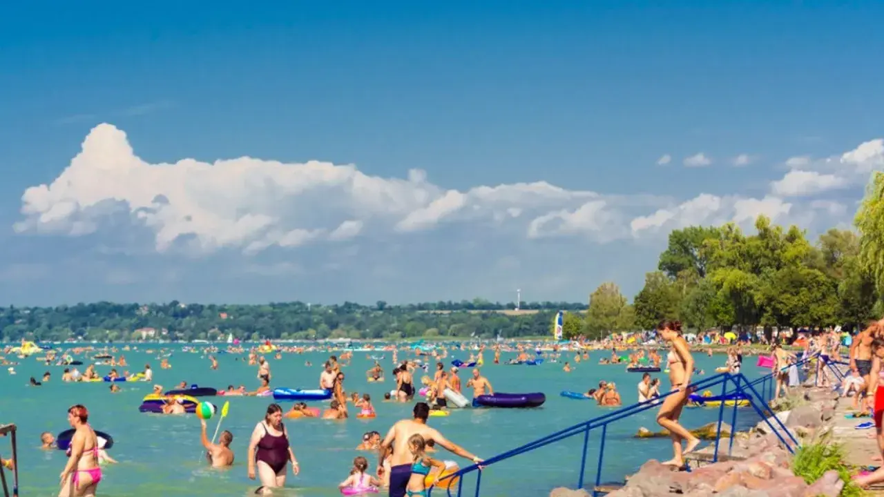Tłum ludzi cieszy się latem na **jeziorze Balaton**. Kąpiel, pływanie na materacach i relaks na plaży.
