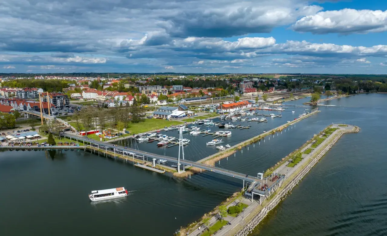 Widok na jezioro, nad którym leży Giżycko, z mariną pełną łodzi, nowoczesnym mostem i spacerowiczami.