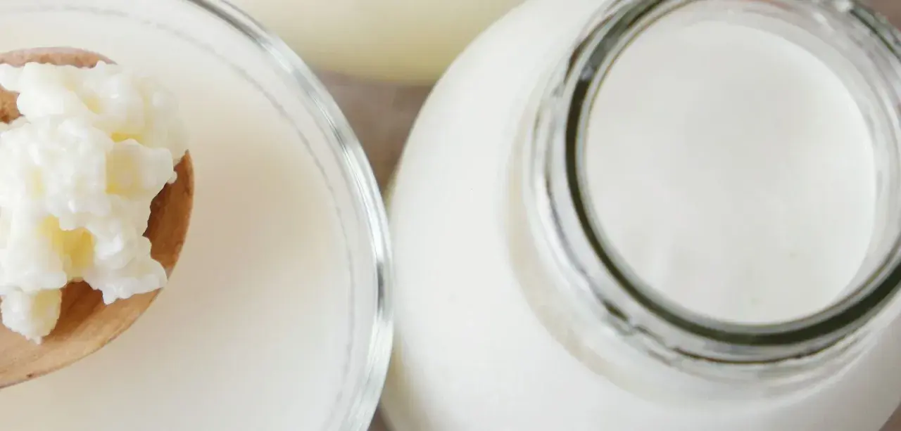 Ziarna żętycy na łyżce obok szklanki i butelki z mlekiem. To naturalny probiotyk.