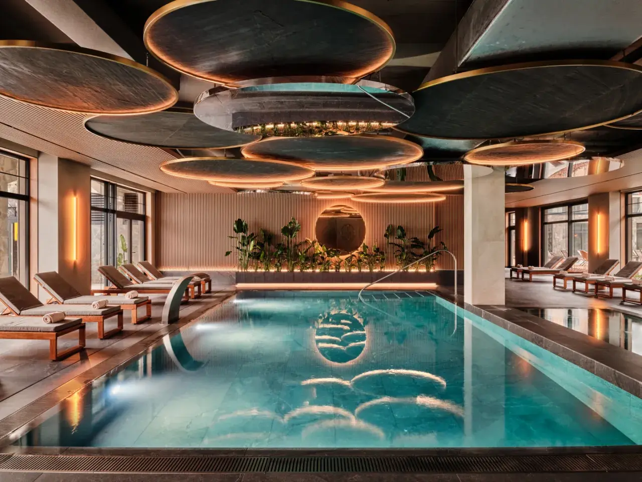 Luksusowy basen w karpacz hotel spa. Woda lśni, otoczona leżakami i zielenią. Nowoczesny design sufitu z podświetleniem.