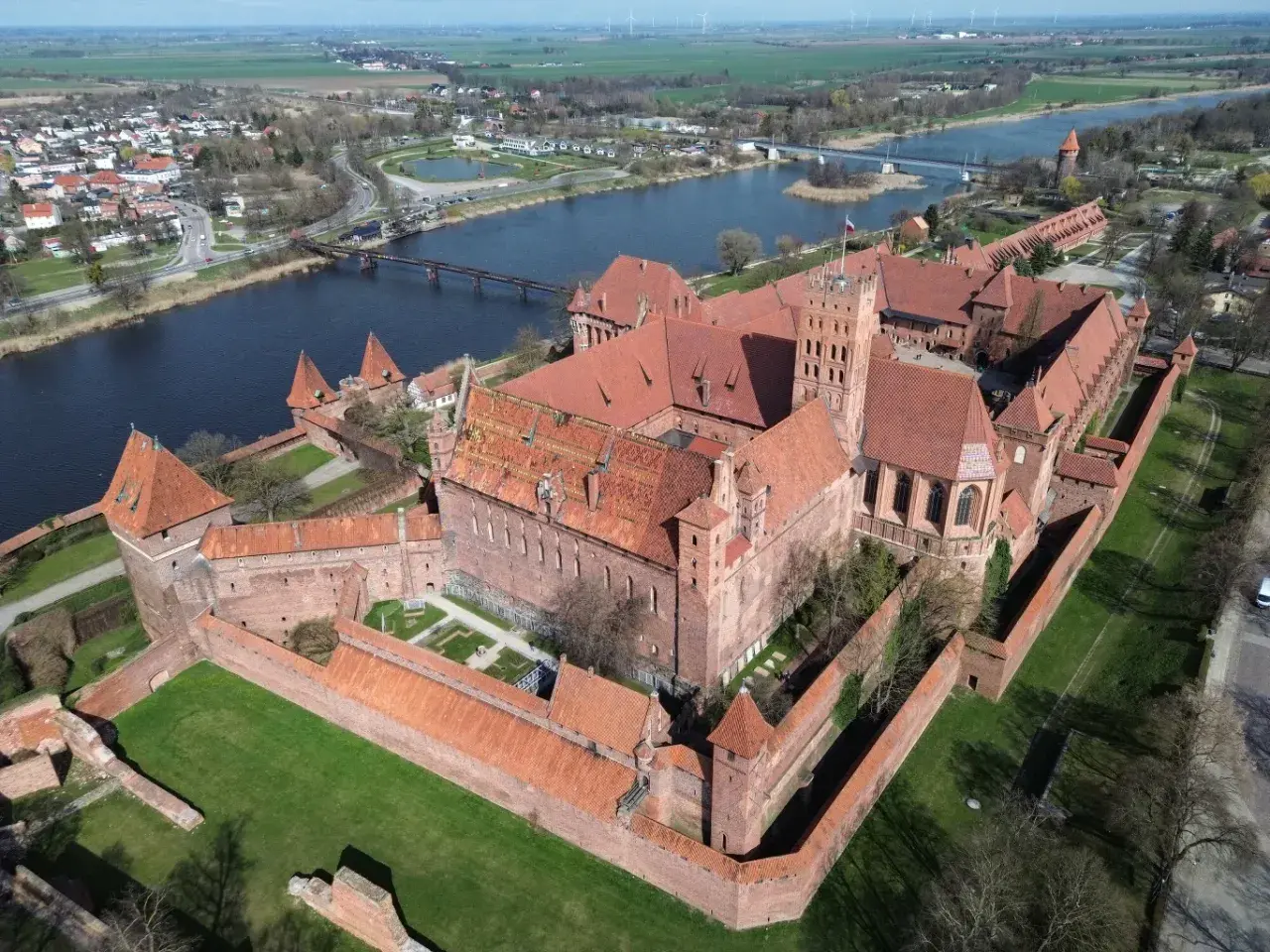 Potężny zamek w Malborku, największy zamek w Europie, rozciąga się wzdłuż rzeki. Jego ceglane mury i wieże świadczą o bogatej historii.