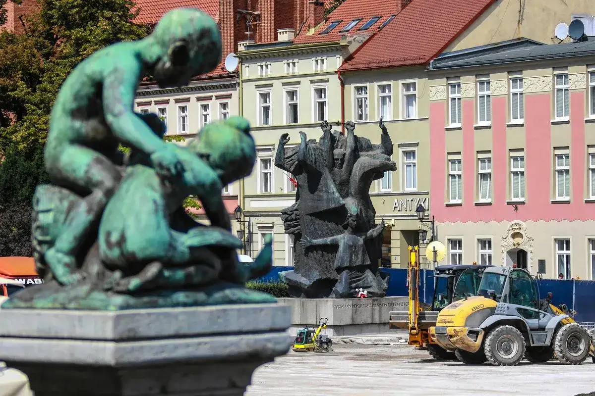 Stary Rynek Bydgoszcz: rzeźba dzieci, pomnik z postaciami i maszyny budowlane na placu.