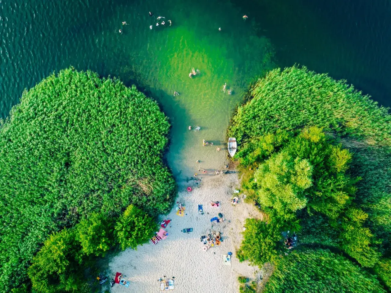 Letnia kąpiel na piaszczystej plaży otoczonej bujną zielenią, woda w jeziorze kusi chłodem. Idealne miejsce na wypoczynek na pojezierzu.