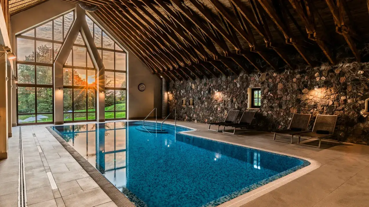 Wnętrze basenu w jednym z hoteli spa Polska. Kamienne ściany, drewniany strop i duże okna z widokiem na zieleń tworzą przytulną atmosferę.