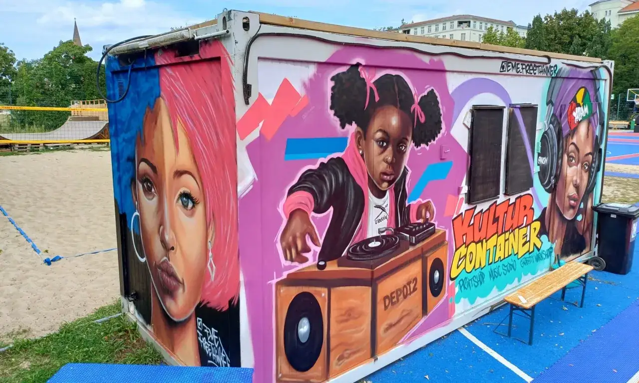 Kolorowy kontener z muralami w stylu Kreuzberg: dziewczyna z różowymi włosami, mała DJ-ka i kobieta w słuchawkach.