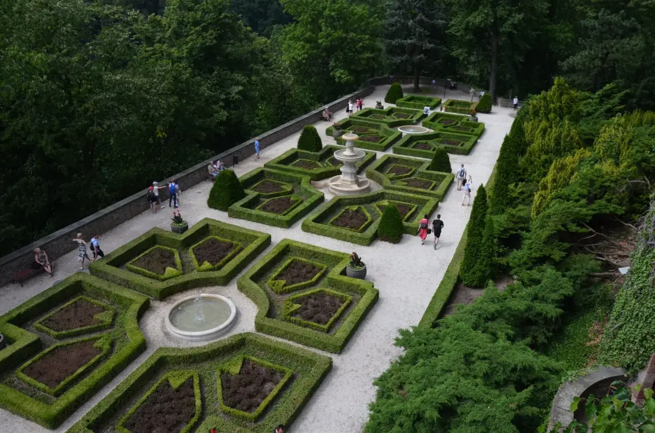 Piękny ogród przy zamku Książ. Wiele osób spaceruje po alejkach, podziwiając geometryczne rabaty i fontanny.